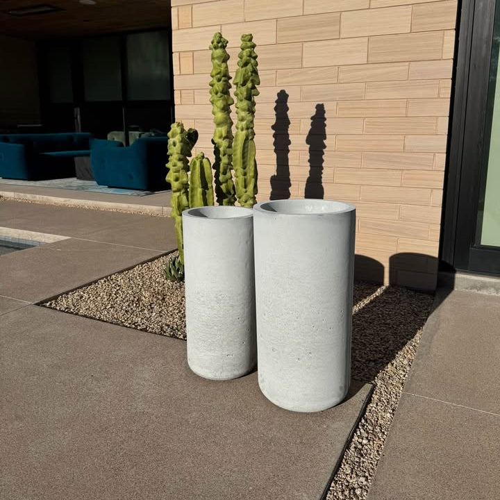 Two cylindrical concrete planters with cacti in front of a building.